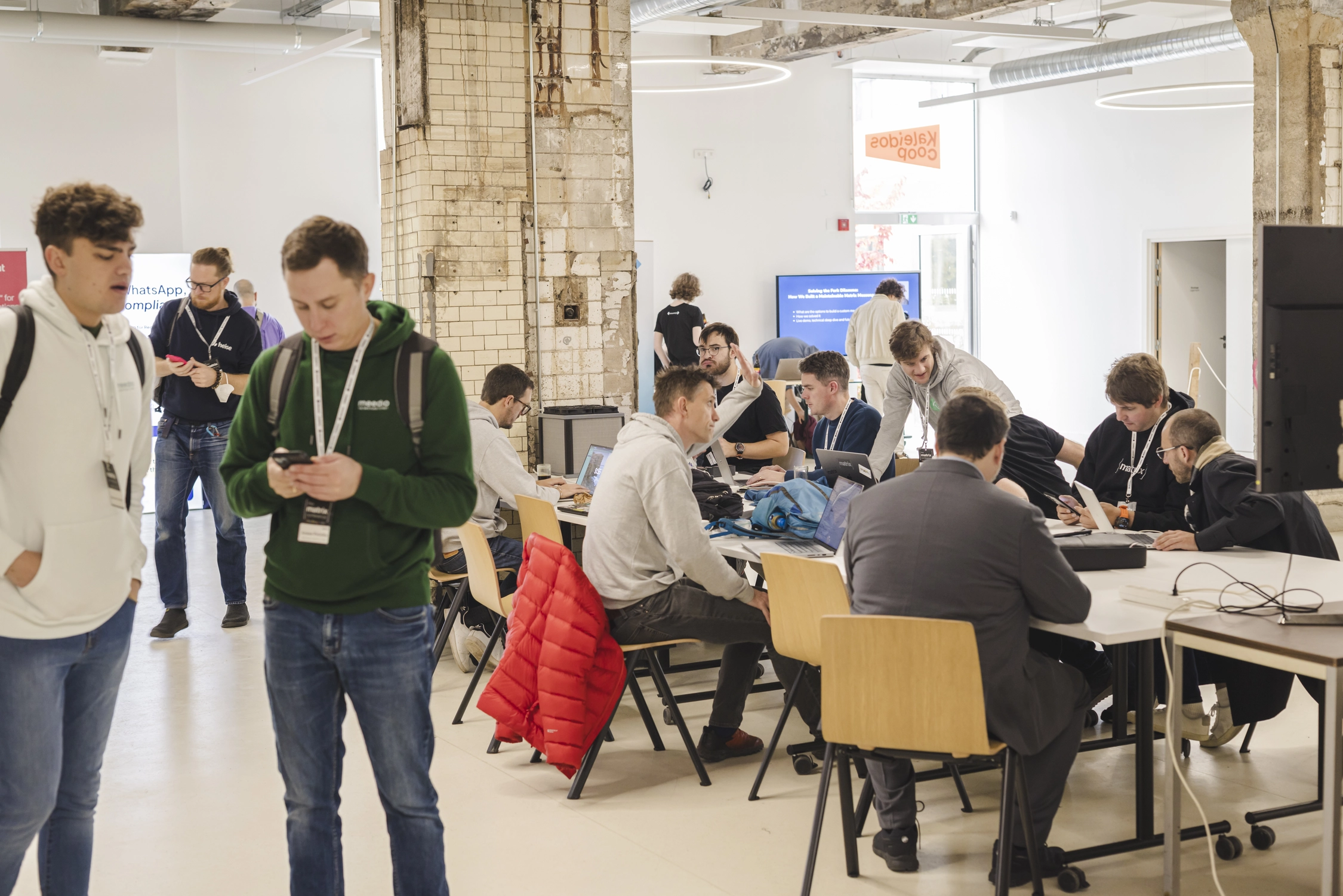 A photo of a people sitting at a table in a busy area, talking to one another and working on their computers.